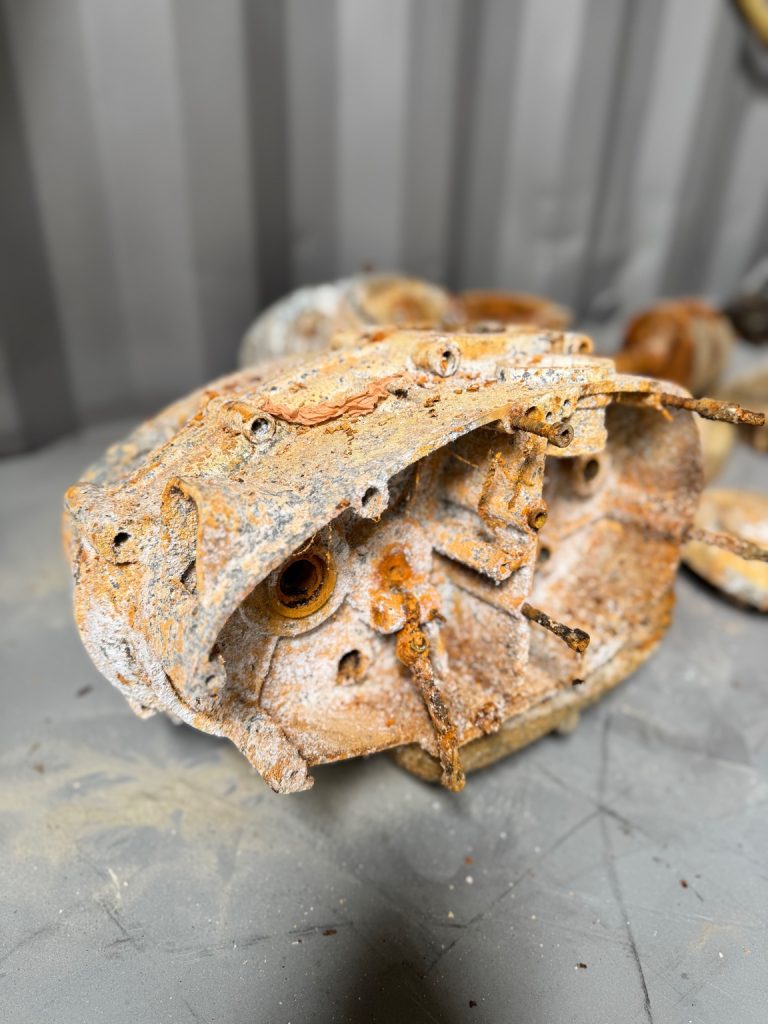 Heavily corroded motorcycle engine casing before vapour blasting next to the same part fully restored with a clean satin finish.