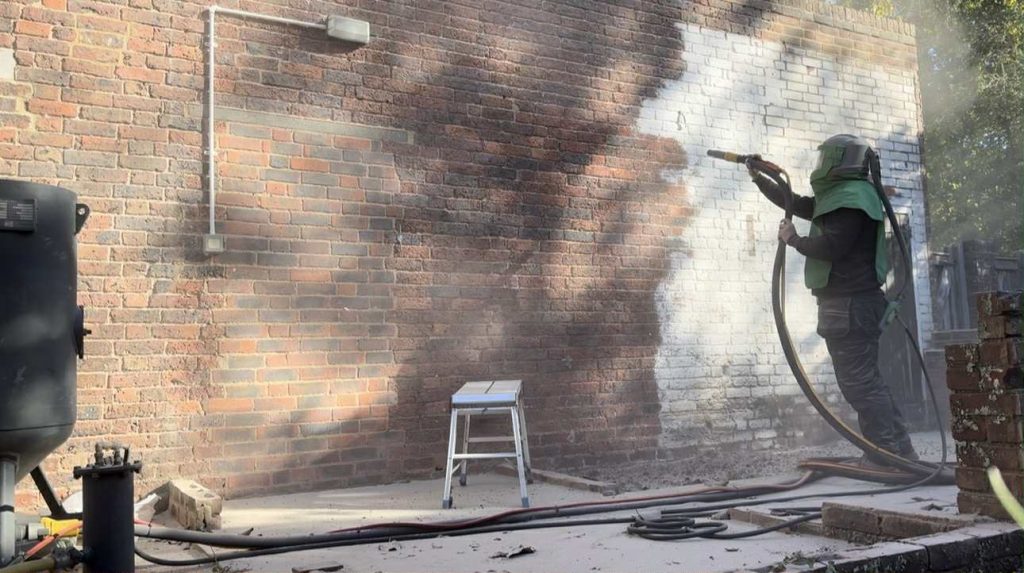 Operator mobile sandblasting paint off a brick wall