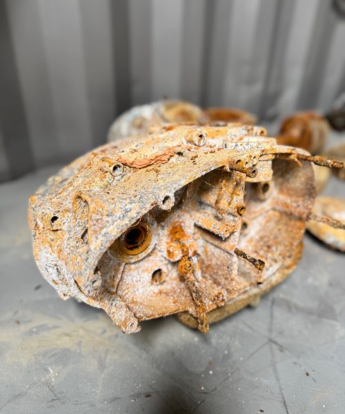 Heavily corroded motorcycle engine casing before vapour blasting next to the same part fully restored with a clean satin finish.